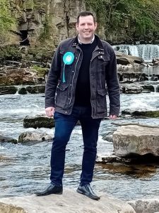 Lee Taylor, PPC for Richmond and Northallerton, standing on rocks by river